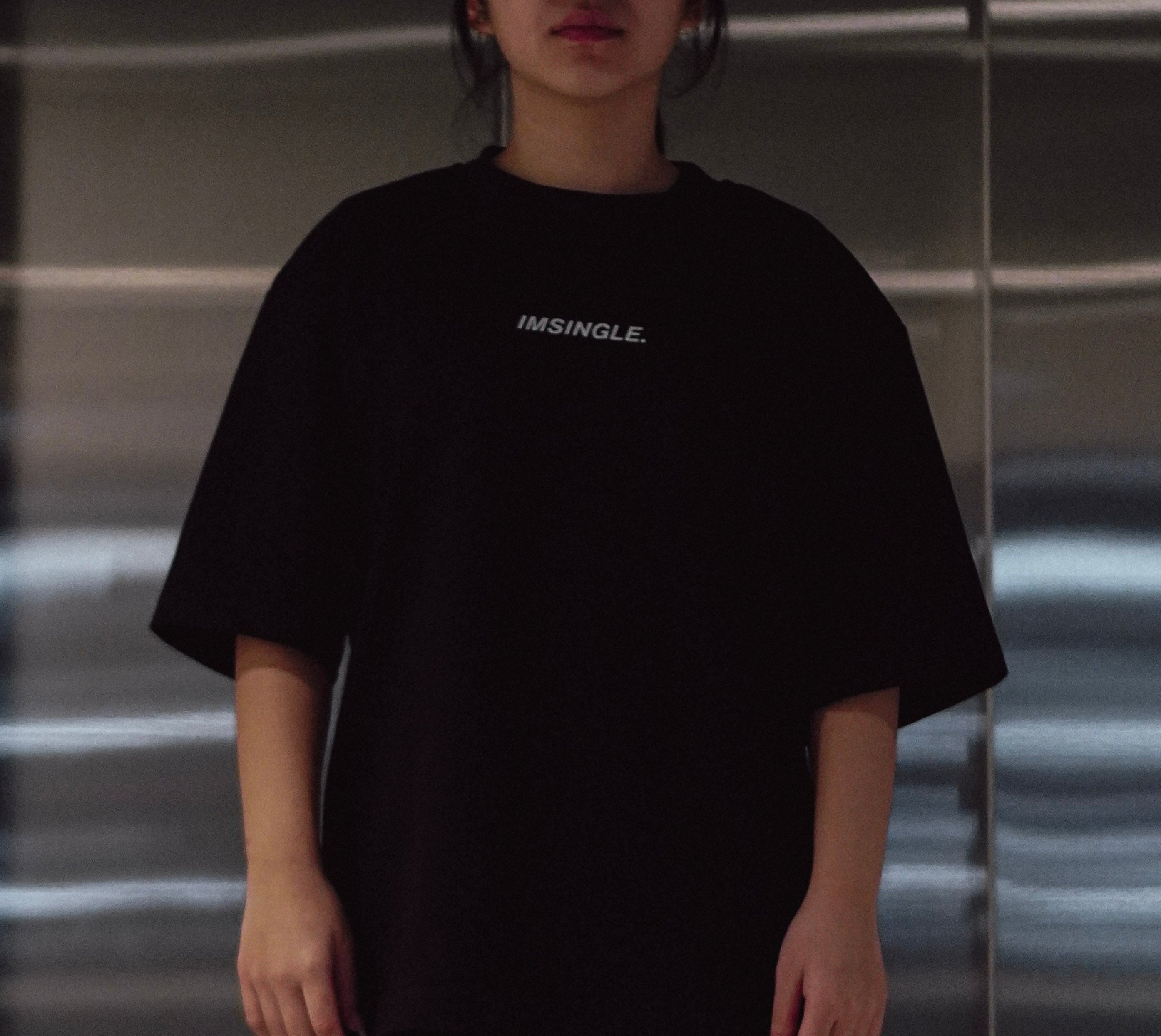 Person wearing a black outfit standing in front of a reflective metallic wall.